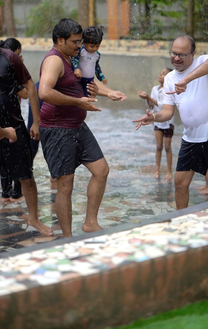 Children in the rain dance area during a birthday celebration, water spraying and music playing