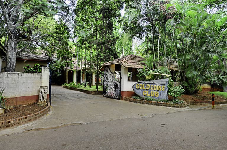 Entrance gate and driveway of Gold Coins Club & Resort seen from Huskur Road
